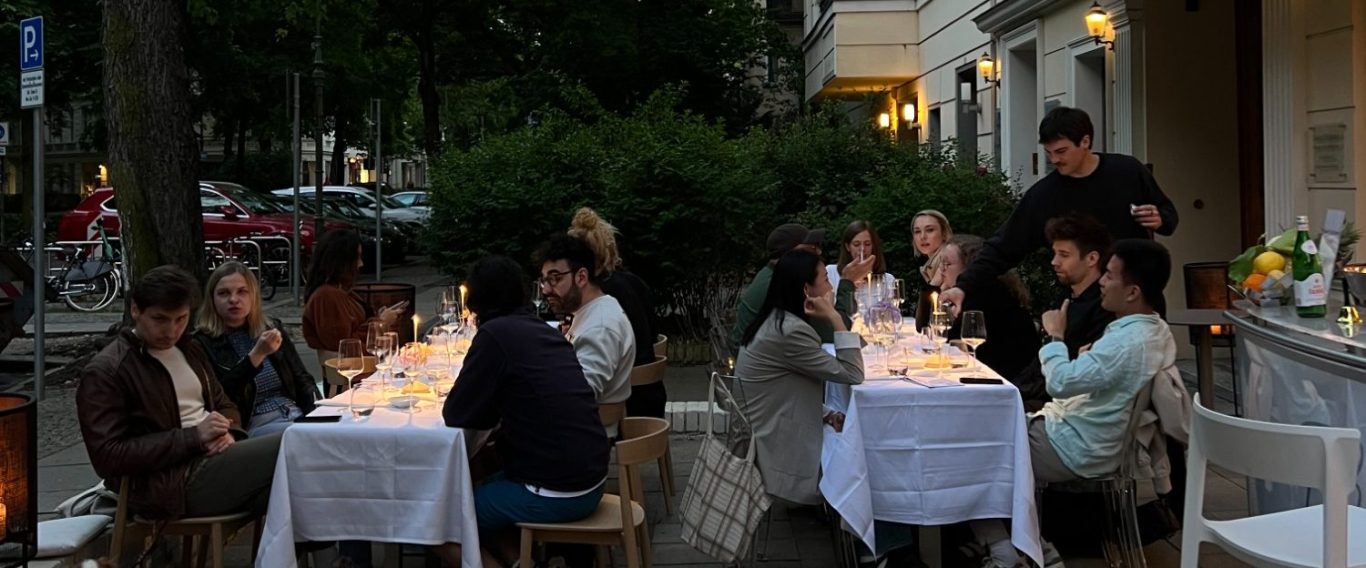 Gruppenevent im Freien bei Dämmerung, Tische mit weißen Tischdecken und Kerzen.